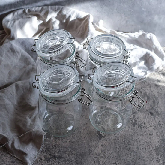 Vier leere 1-Liter-Bügelgläser stehen auf Leinentuch und Steinfläche und eignen sich ideal zum Fermentieren und zur Vorratshaltung