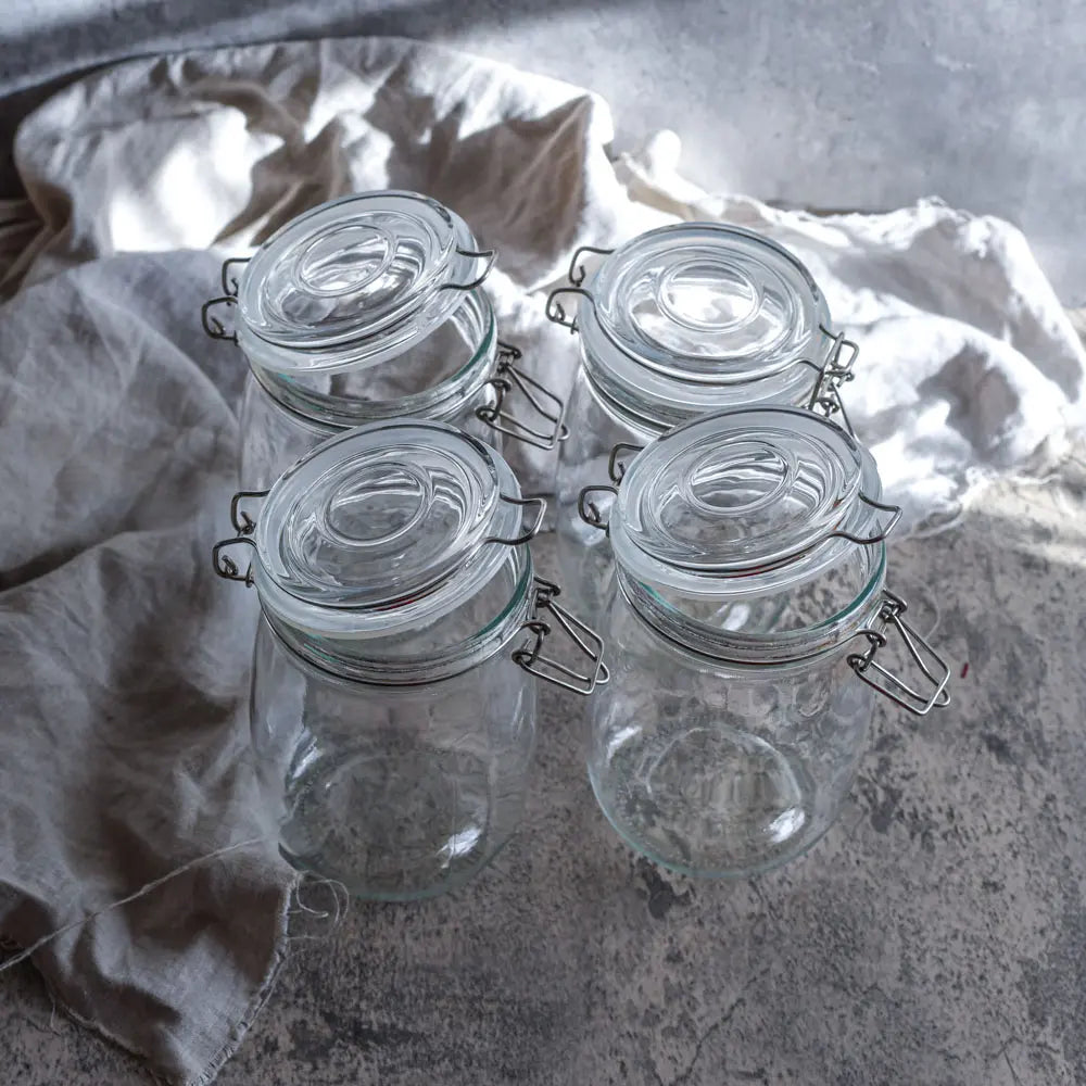 Vier leere 1-Liter-Bügelgläser stehen auf Leinentuch und Steinfläche und eignen sich ideal zum Fermentieren und zur Vorratshaltung