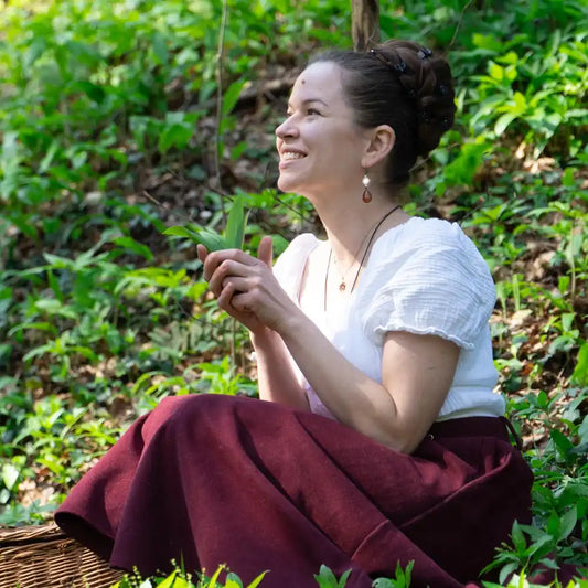 Frau sitzt im Wald und hält frischen Bärlauch in den Händen, lächelt in die Natur, achtsames Sammeln von Wildkräutern im Frühling.