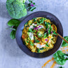 Veganes Brokkoli-Curry mit Gemüse, Kräutern und cremiger Sauce in dunkler Schüssel auf grauem Hintergrund.