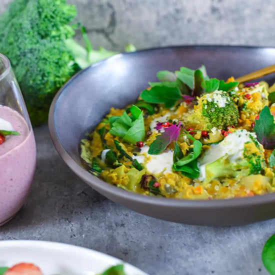 Cremiges veganes Brokkoli-Gemüse-Curry mit frischen Kräutern und Gemüse in dunkler Schüssel serviert.
