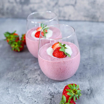 Cremiges veganes Erdbeer-Dessert in zwei Gläsern mit frischen Erdbeeren dekoriert auf grauem Hintergrund