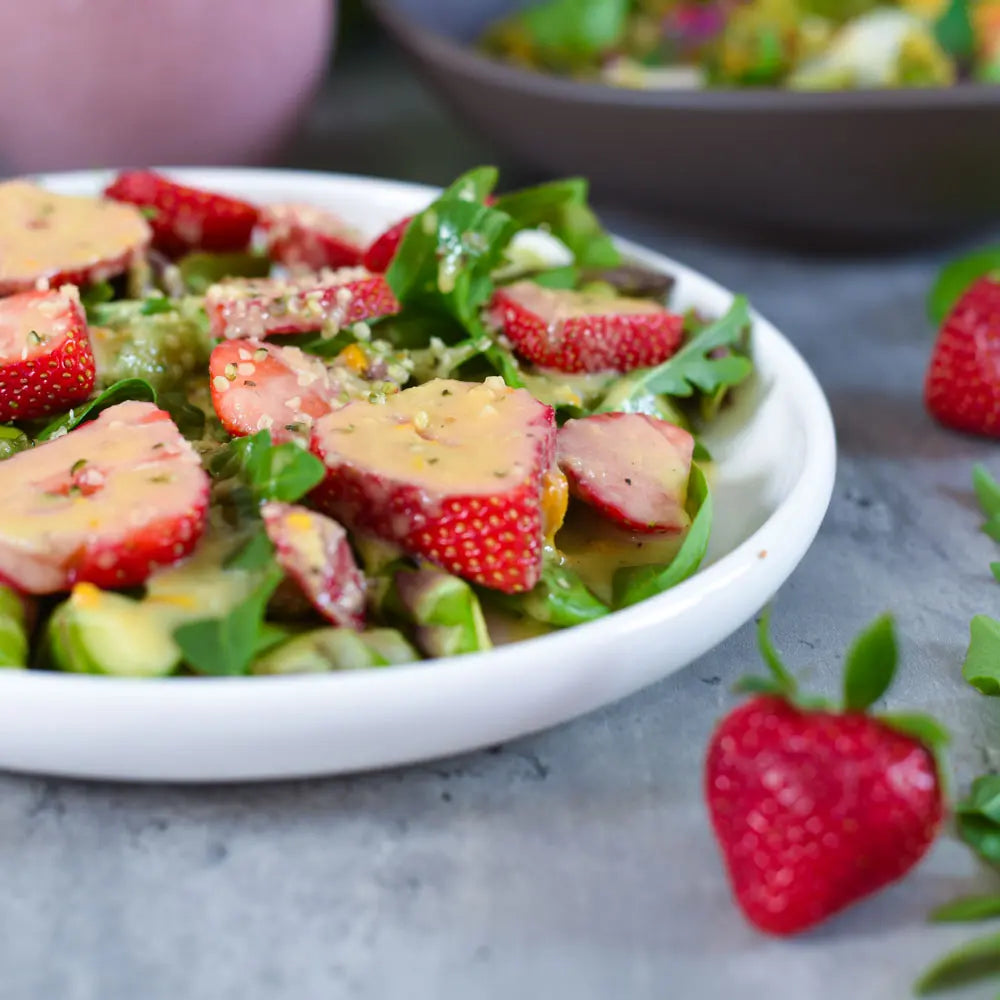Frischer veganer Erdbeer-Salat mit grünem Salat und cremigem Dressing auf hellem Teller angerichtet.