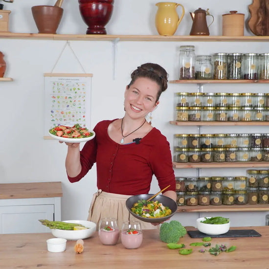 Lächelnde Frau präsentiert vegane Frühlingsgerichte mit frischem Gemüse und gesunden Zutaten in natürlicher Küche.