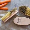 Gemüsebürsten aus Holz mit Naturborsten neben Karotten auf Stoff und grauer Oberfläche – ideal zum Reinigen von Gemüse in der Küche.