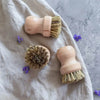 Mehrere Holzbürsten mit Naturborsten auf Stoff und grauer Oberfläche mit kleinen violetten Blüten – ideal für Küche und Haushalt.