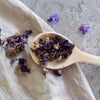 Detailaufnahme eines Holzkochlöffels mit getrockneten Blüten auf Stoff – dekorativ und ideal für Küche und Food Styling