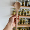 Holzkochlöffel wird in der Hand gehalten vor Regal mit Gläsern – ideal zum Kochen und Umrühren in der Küche.