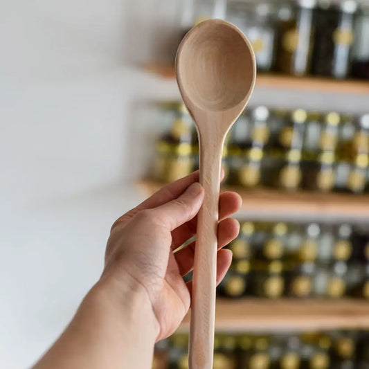 Holzkochlöffel wird in der Hand gehalten vor Regal mit Gläsern – ideal zum Kochen und Umrühren in der Küche.