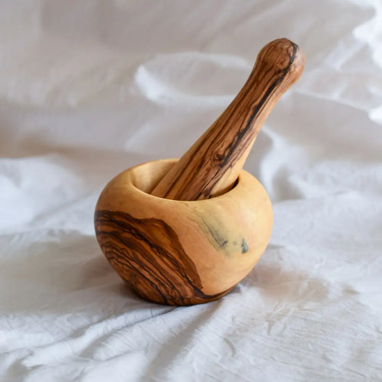 Mörser und Stößel aus Olivenholz auf hellem Stoffhintergrund – schlichtes, natürliches Küchenutensil zum Mahlen von Gewürzen.