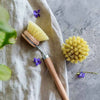 Spülbürste aus Holz mit Wechselkopf und Naturborsten auf Stoff mit kleinen violetten Blüten – ideal für Küche und Haushalt.