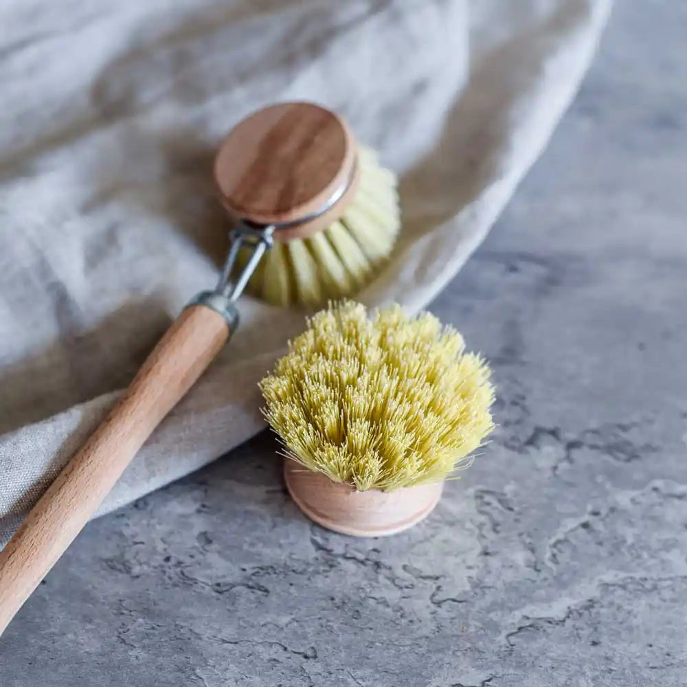 Spülbürste aus Holz mit Wechselkopf und Naturborsten auf Stoff und grauer Oberfläche – ideal zum Reinigen von Geschirr.