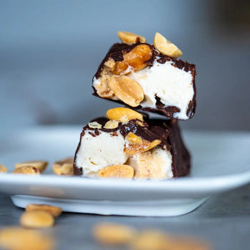 Aufgeschnittener veganer Eisriegel mit Schokolade, cremigem Eis, Karamell und gerösteten Erdnüssen auf einem Teller.