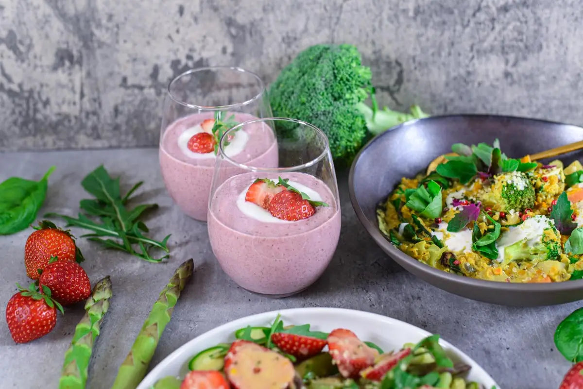 Vegane Frühlingsgerichte mit Erdbeer-Salat, cremigem Curry und Erdbeer-Dessert auf grauem Hintergrund angerichtet.