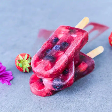 Veganes Beeren-Stieleis mit Erdbeeren und Heidelbeeren, dekoriert mit frischen Erdbeeren und einer Blüte.