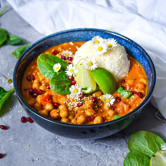 Vegane Bowl mit cremigem Kichererbsen-Curry, Reis, Limette, Spinat, Granatapfelkernen und essbaren Blüten.