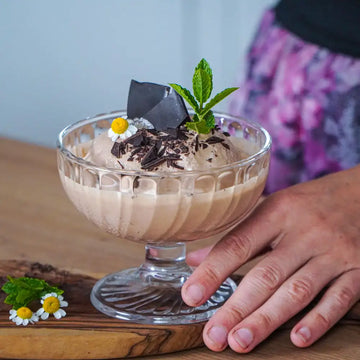 Cremiges veganes Schokoladeneis mit Schokostückchen, Minze und Kamillenblüten in einer gläsernen Dessertschale.