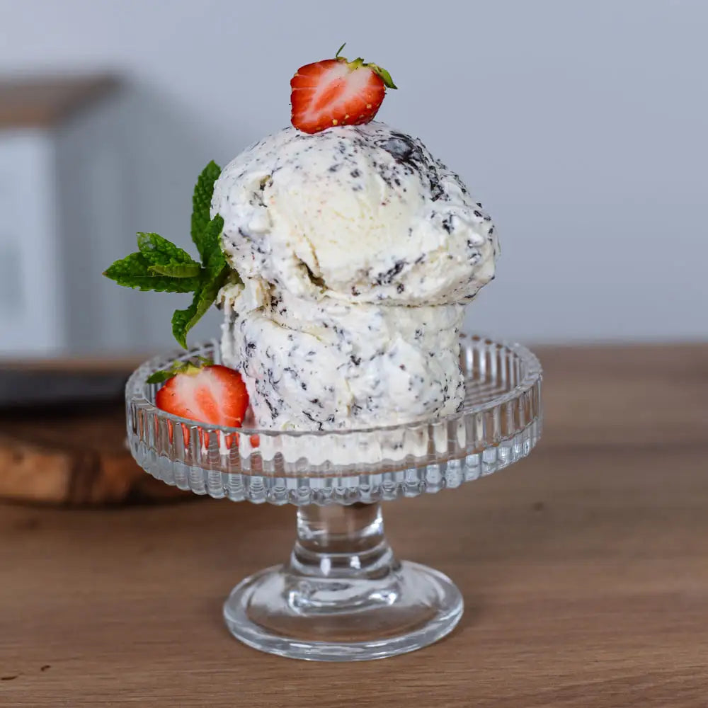 Cremiges veganes Stracciatella-Eis mit Schokostückchen, Erdbeeren und Minze auf einer gläsernen Dessertschale.