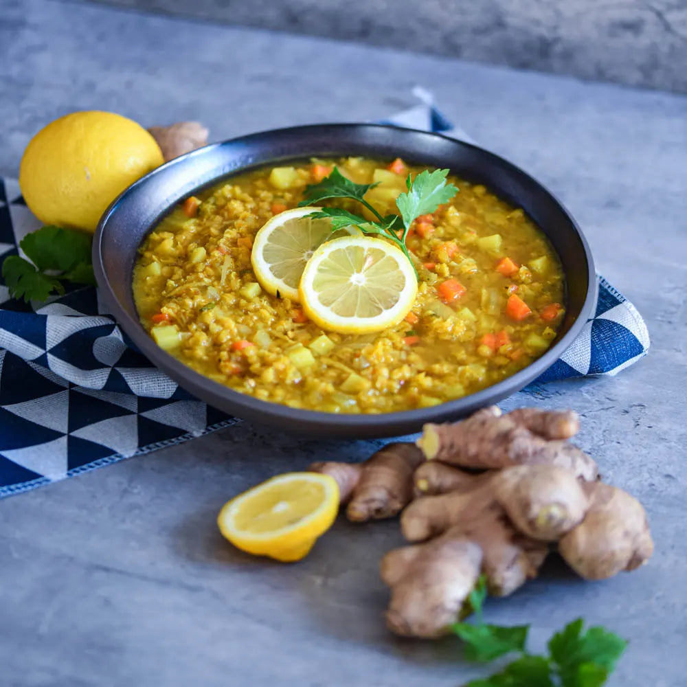 Vegane Ingwer-Linsen-Suppe mit Gemüse und Zitronenscheiben, serviert in schwarzer Schale, nährend und wärmend.