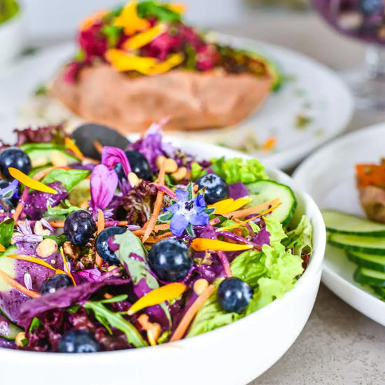 Farbenfroher Sommersalat mit Heidelbeeren, Gurken, essbaren Blüten und frischen Kräutern als nährstoffreiche pflanzliche Mahlzeit.