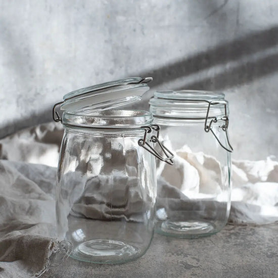 Zwei leere Drahtbügelgläser stehen im weichen Licht auf Leinenstoff, bereit für frisches Gemüse und selbstgemachte Fermente.