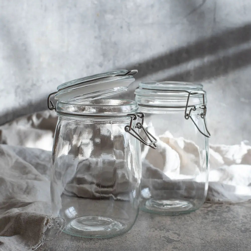 Zwei leere Drahtbügelgläser stehen im weichen Licht auf Leinenstoff, bereit für frisches Gemüse und selbstgemachte Fermente.