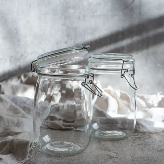 Zwei leere Drahtbügelgläser stehen im weichen Licht auf Leinenstoff, bereit für frisches Gemüse und selbstgemachte Fermente.