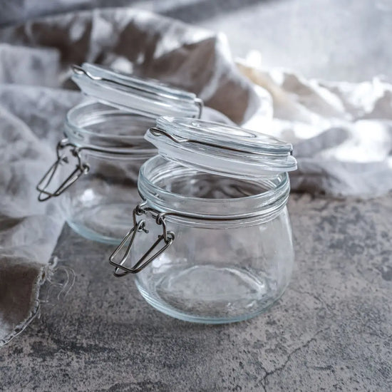 Zwei leere 500-ml-Drahtbuegelglaeser stehen im weichen Licht auf Leinenstoff bereit fuer neue Fermente, kleine Vorräte oder mealprep.