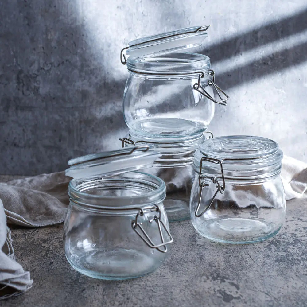 Drei leere 500-ml-Drahtbuegelglaeser stehen im weichen Licht auf Leinenstoff bereit fuer neue Fermente oder kleine Vorräte.