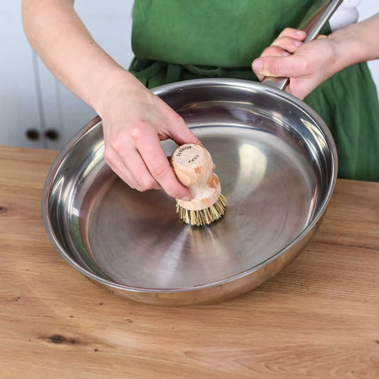Reinigung einer Edelstahlpfanne mit einer nachhaltigen Holzbürste in der Küche für eine natürliche und plastikfreie Küchenpflege