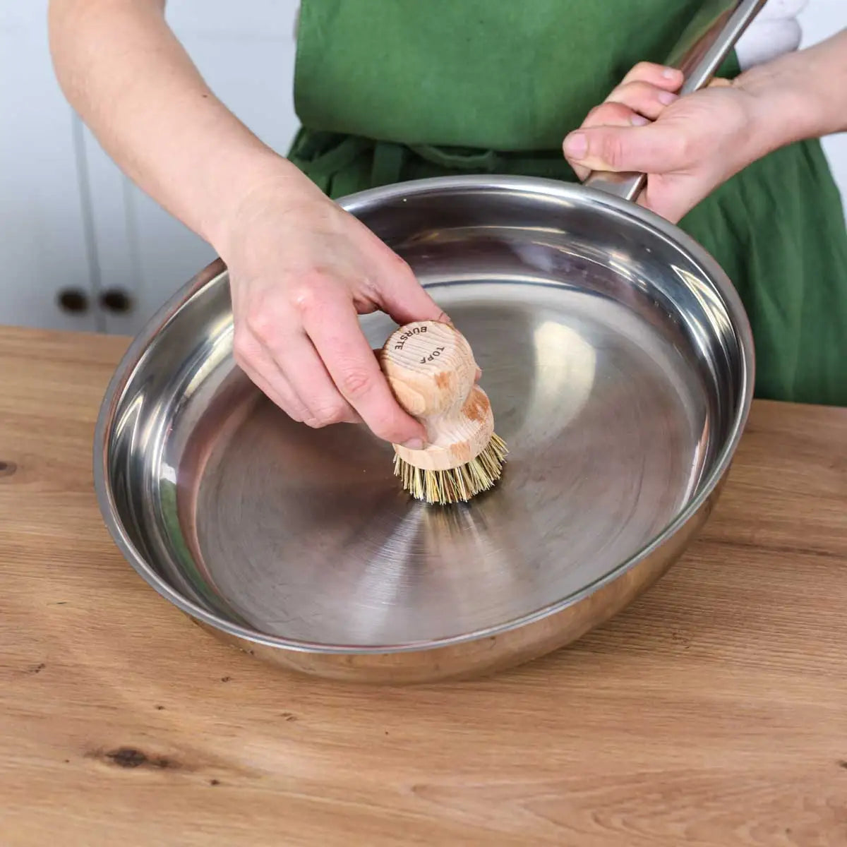 Reinigung einer Edelstahlpfanne mit einer nachhaltigen Holzbürste in der Küche für eine natürliche und plastikfreie Küchenpflege