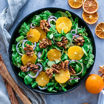 Schüssel mit Feldsalat, Orangenringen, roten Zwiebeln und Walnüssen, umgeben von Orangen und getrockneten Orangenscheiben.