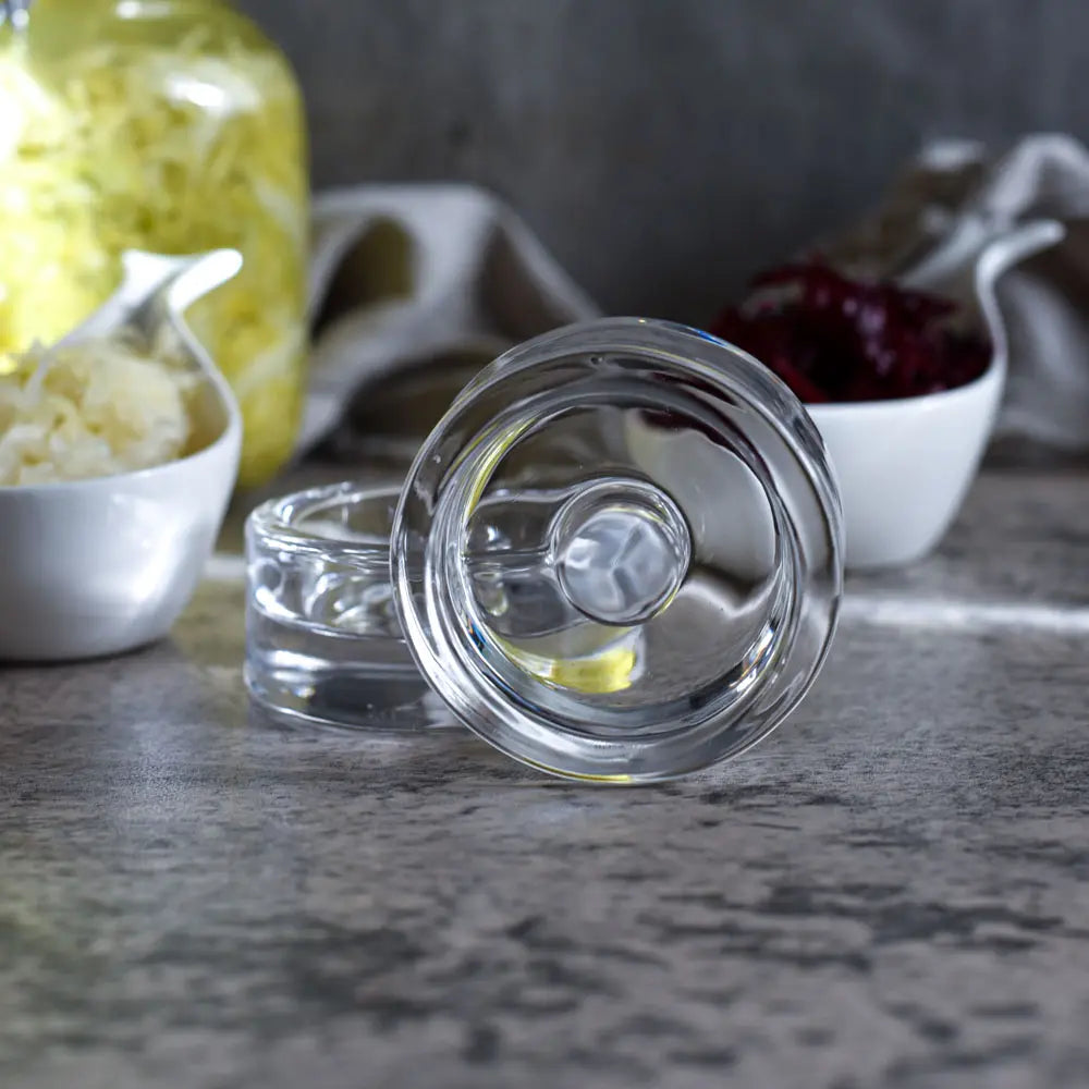 Glasgewichte für Fermentation liegen vor Sauerkraut und Rotkraut in kleinen Schalen auf dem Tisch.