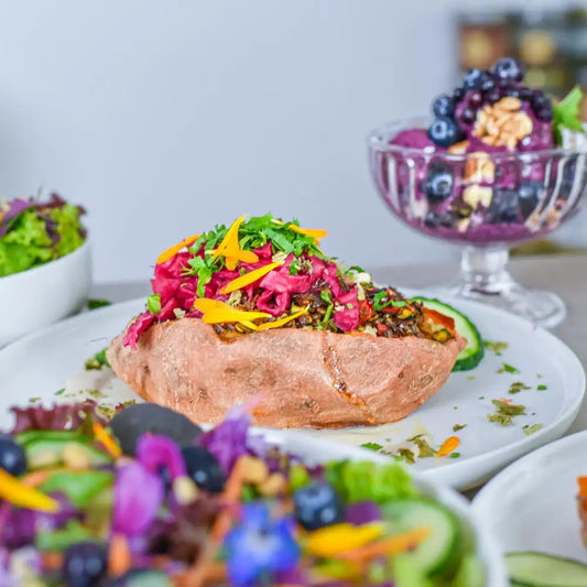 Gefüllte Süßkartoffel mit würziger Linsenfüllung, Rotkrautsalat, frischen Kräutern und essbaren Blüten als gesundes Sommergericht.