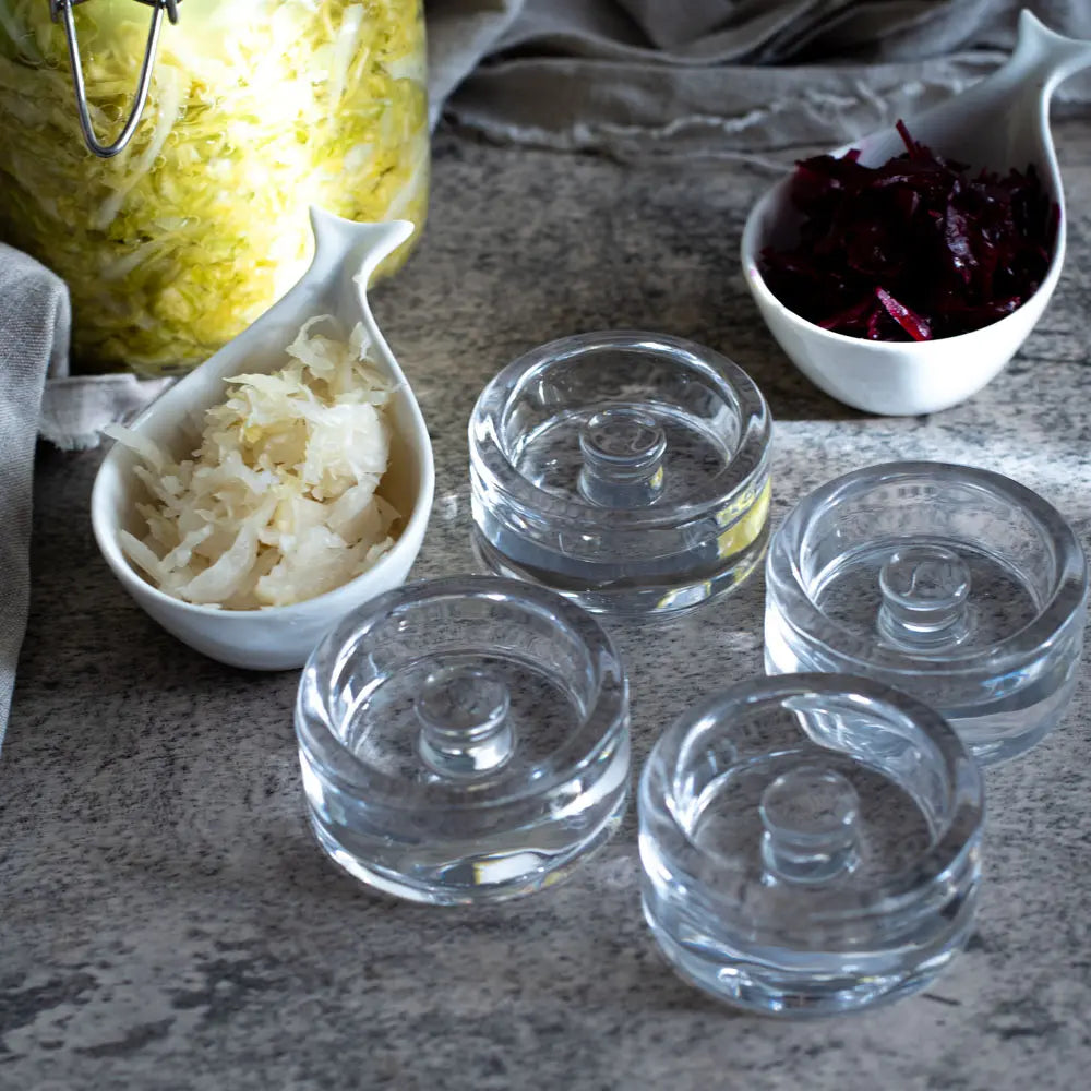 Vier Glasgewichte für Fermentation neben Sauerkraut und Rotkraut
