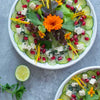 Draufsicht auf zwei Teller Gurken-Carpaccio mit Feta, Granatapfelkernen, Blattsalat und Blüten dekoriert.