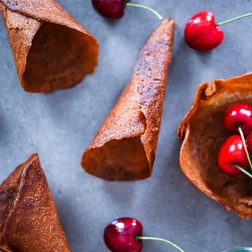 Knusprige Karamell-Waffeltüten liegen auf grauem Untergrund neben frischen Kirschen.