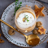 Glas mit cremiger Kastaniensuppe und Schaum, dekoriert mit Kräutern, dazu goldener Löffel und sternförmige Brotstücke auf einem Teller.