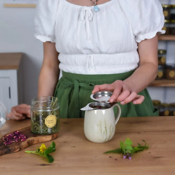 Loser Kräutertee wird in einem Edelstahl-Teesieb in einer Teetasse aufgegossen und anschließend mit einem Deckel abgedeckt.