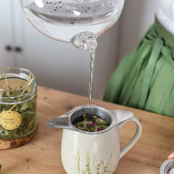 Heißes Wasser wird über eine Kräuterteemischung in einem Teesieb gegossen.
