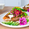 Gebackene Süßkartoffel mit Linsen, Kräutern, Rotkrautsalat und essbaren Blüten als pflanzliche Longevity-Mahlzeit im Sommer.