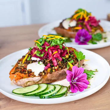 Gebackene Süßkartoffel mit Linsen, Kräutern, Rotkrautsalat und essbaren Blüten als pflanzliche Longevity-Mahlzeit im Sommer.
