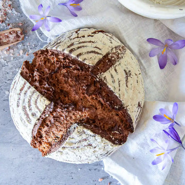 Aromatisches rustikales Sauerteigbrot mit knuspriger Kruste, dekoriert mit Blumen auf Leinentuch.