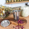 Edelstahl-Teesieb mit getrockneten Rosenblüten für die Zubereitung von losem Kräutertee.