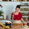 Eine Frau steht an einer veganen Weihnachtstafel mit Festtagsgerichten, Rotkraut, Knödeln und einem weihnachtlichen Getränk.