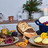Vegane Festtagstafel mit Nussbraten im Blätterteig, Rotkraut, Knödeln und weihnachtlicher Dekoration im Hintergrund.