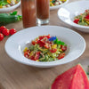 Schale mit Zucchininudeln, Cherrytomaten und Pinienkernen, im Hintergrund Drinks, weitere Salate und Wassermelone.